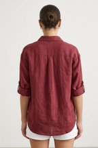 Person wearing a burgundy shirt with rolled-up sleeves on a white background