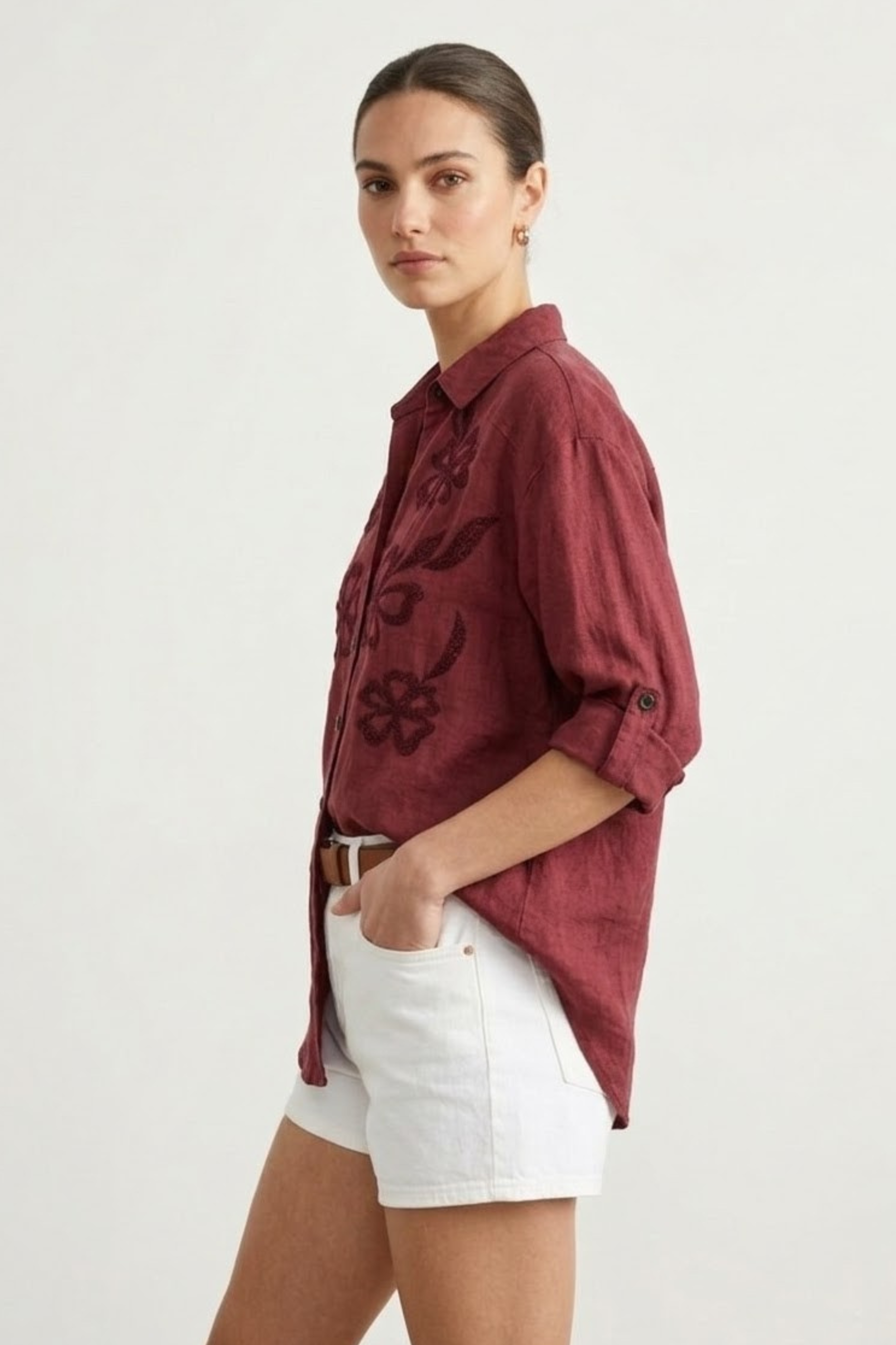 Woman wearing a burgundy floral shirt and white shorts on a white background