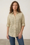 Woman wearing a beige patterned shirt and blue jeans against a plain background