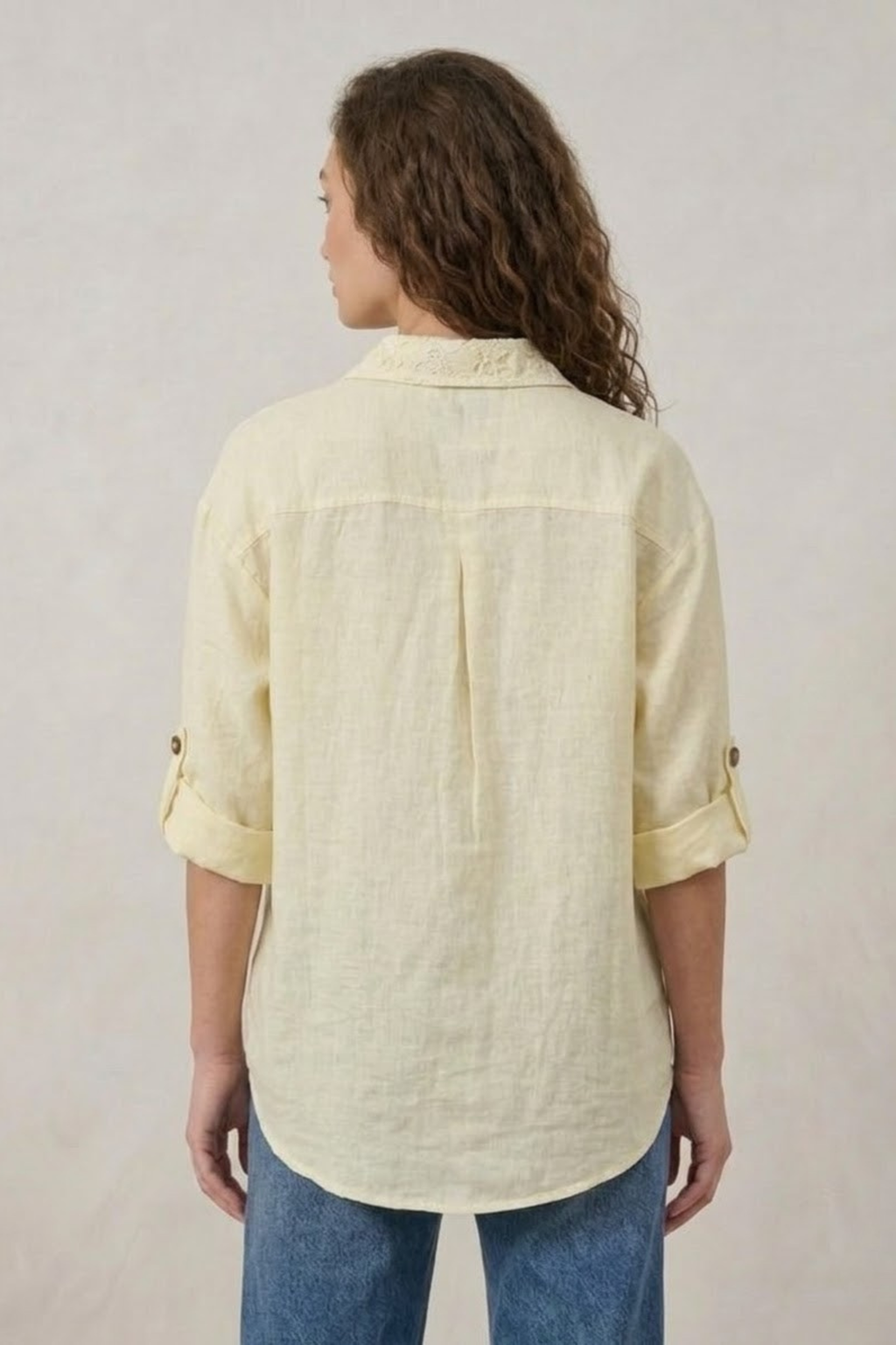 Woman wearing a light yellow shirt and blue jeans on a plain background