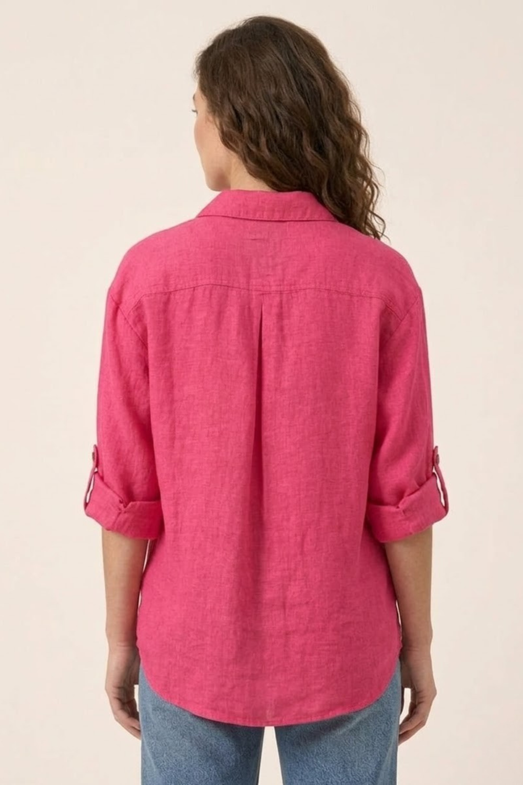Person wearing a pink shirt with rolled-up sleeves on a beige background