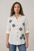 Woman wearing a white shirt with blue floral patterns on a plain background