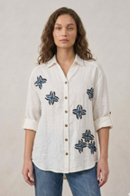 Woman wearing a white shirt with blue floral patterns on a plain background