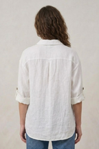 Person wearing a white textured shirt with rolled-up sleeves on a plain background