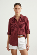 Woman wearing a burgundy embroidered shirt and white shorts on a plain background