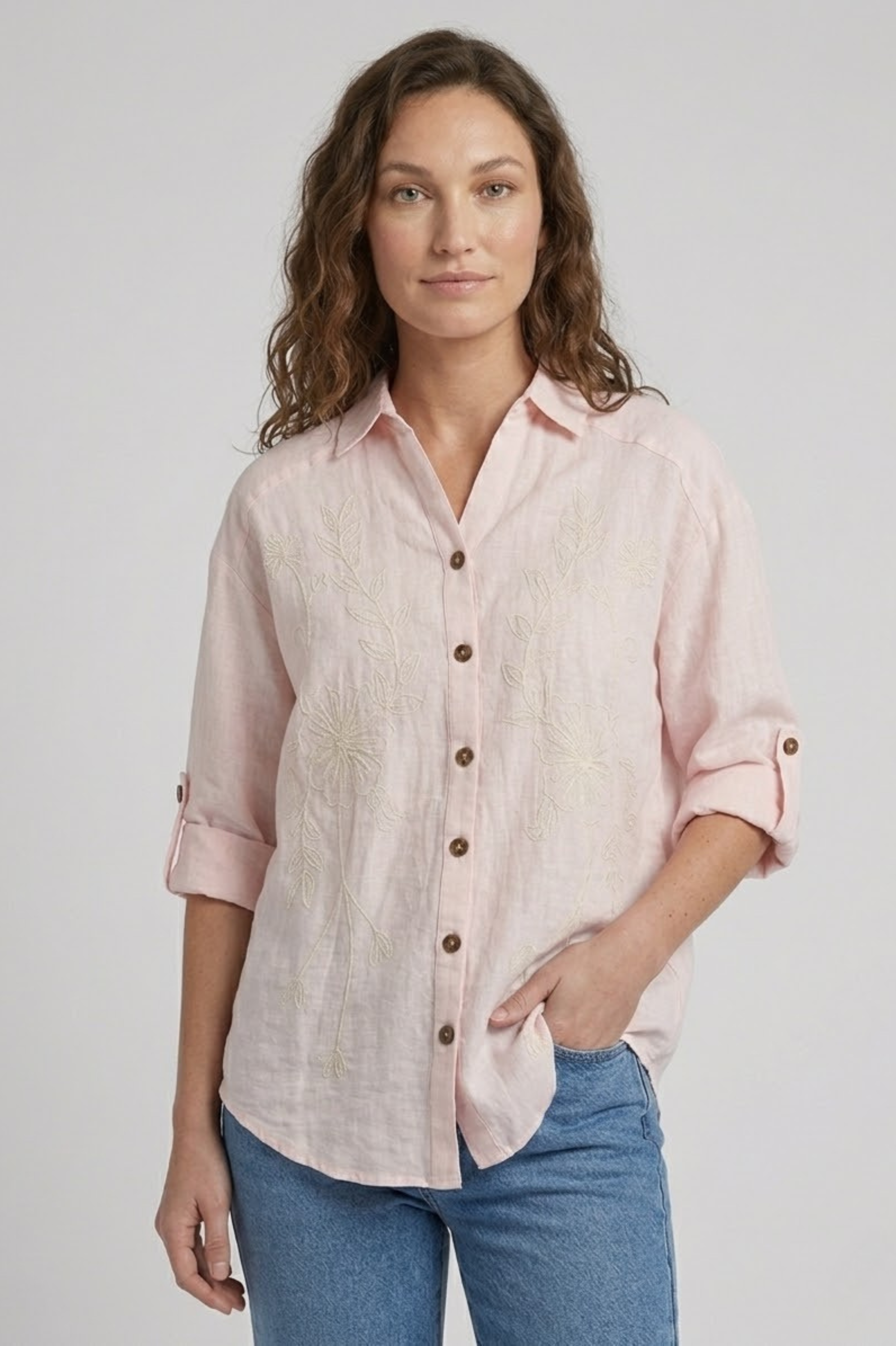Woman wearing a light pink button-up shirt and blue jeans on a plain background