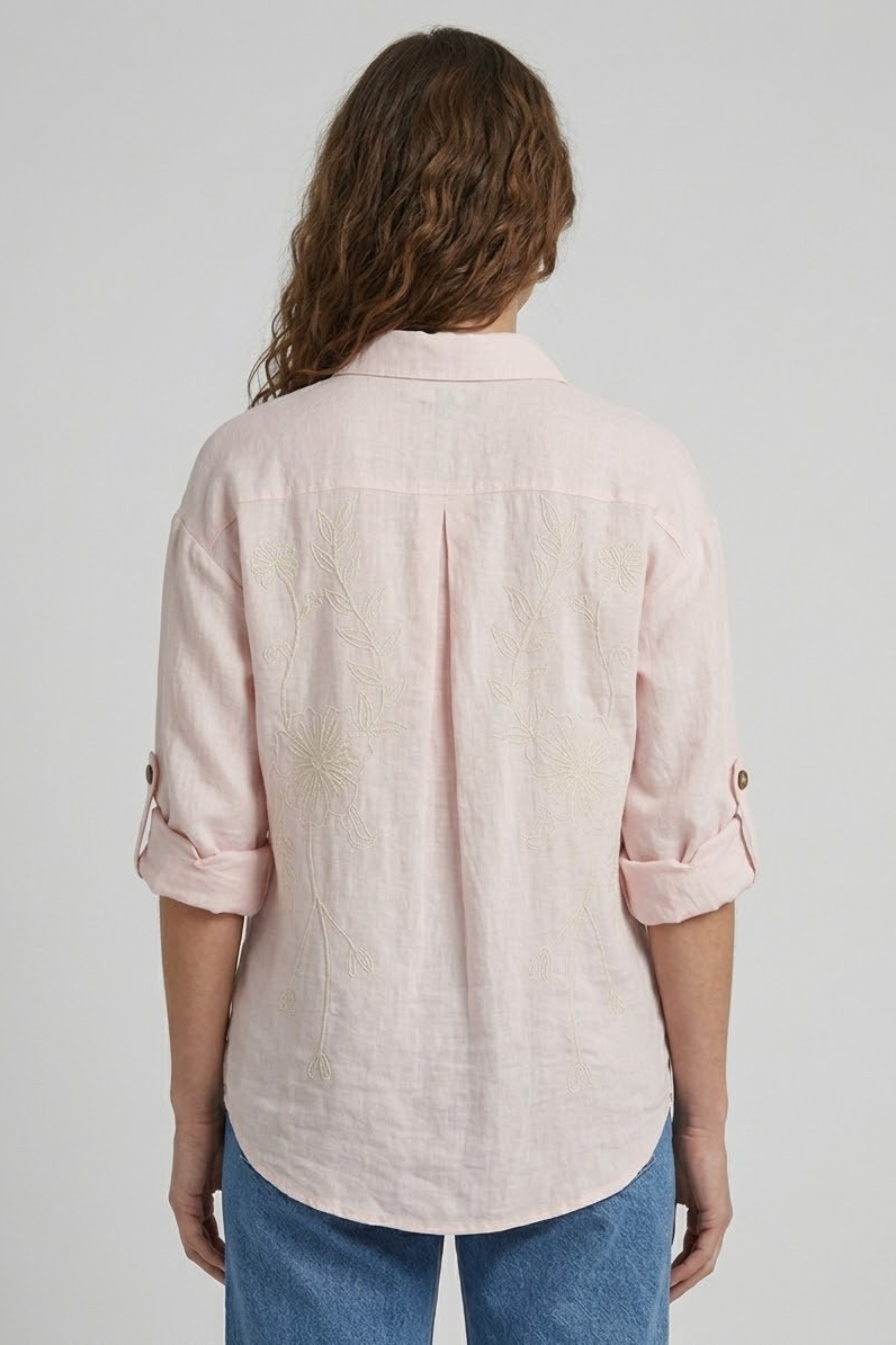 Person wearing a light pink shirt and blue jeans on a plain background
