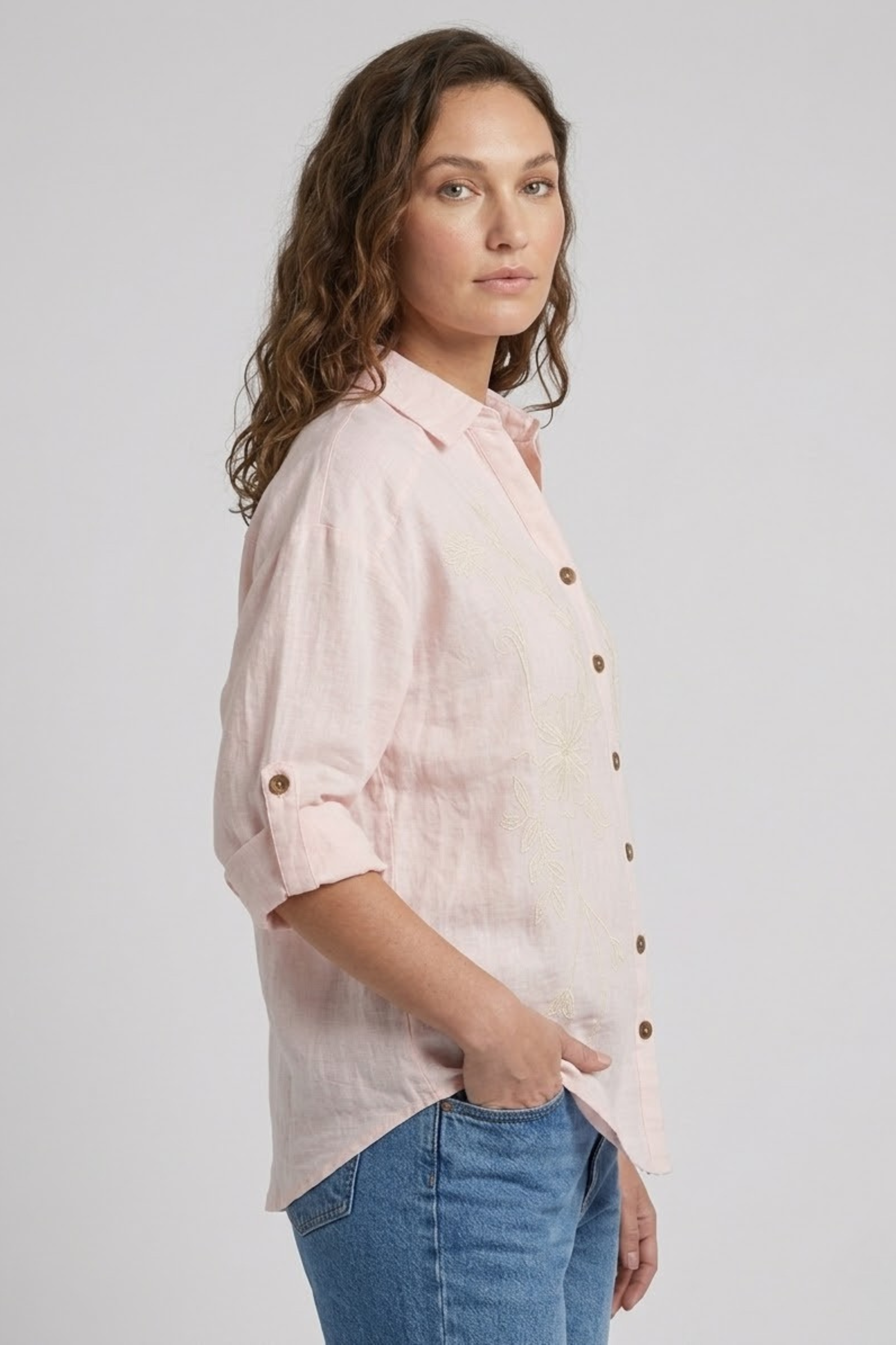 Woman wearing a light pink button-up shirt and blue jeans on a plain background