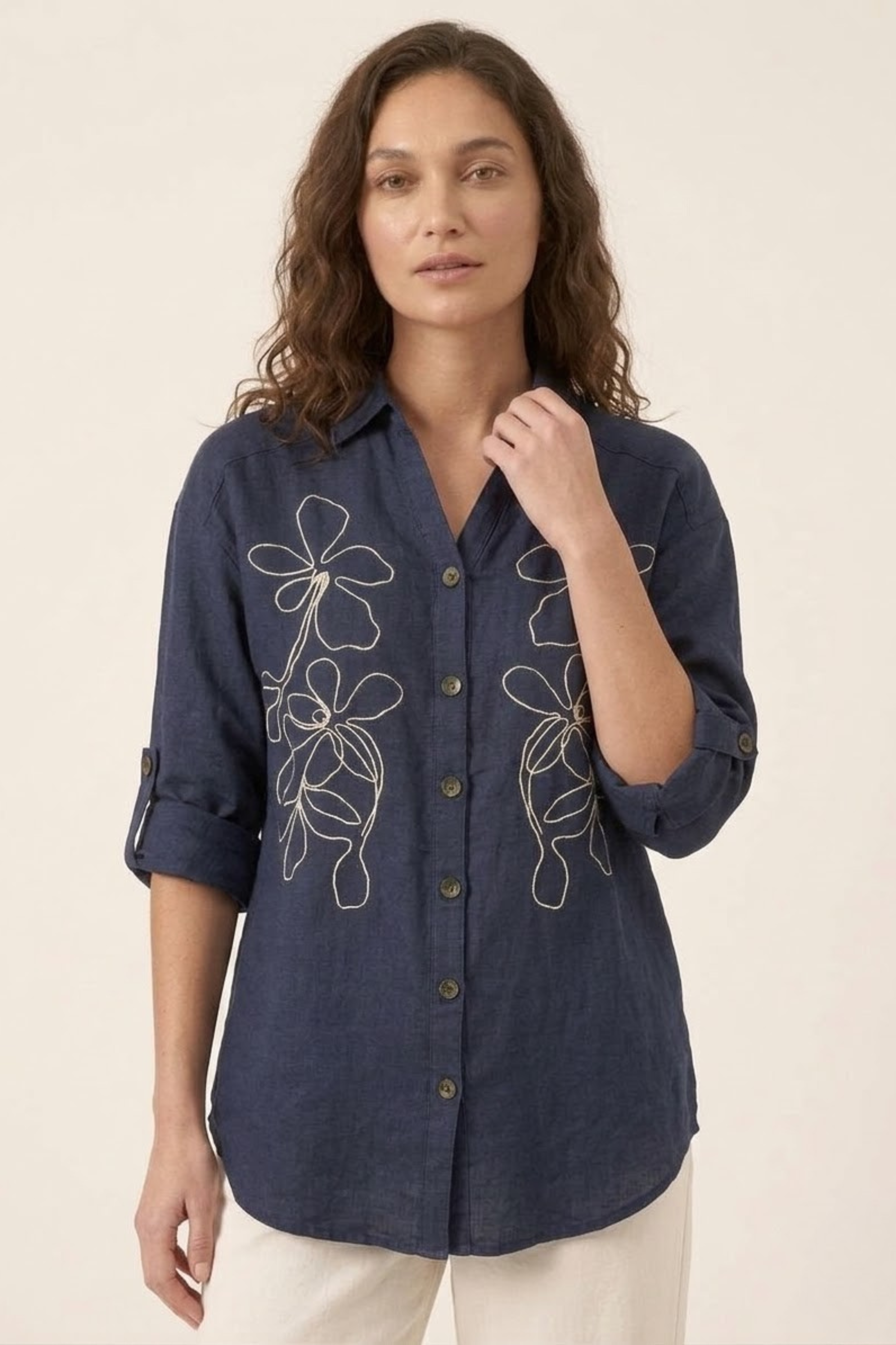 Woman wearing a navy blue shirt with floral embroidery on a beige background