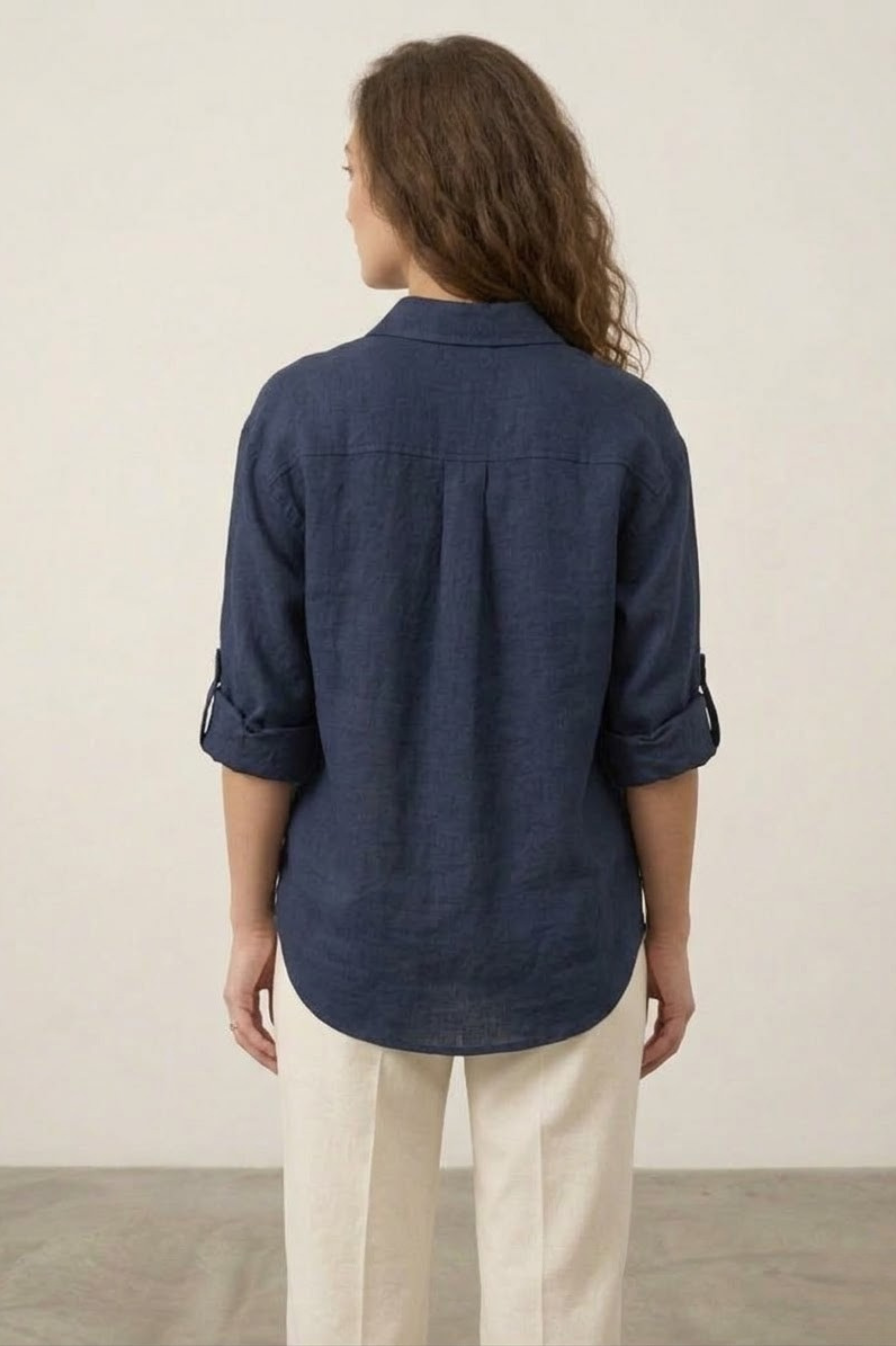 Person wearing a navy blue shirt and beige pants against a plain background