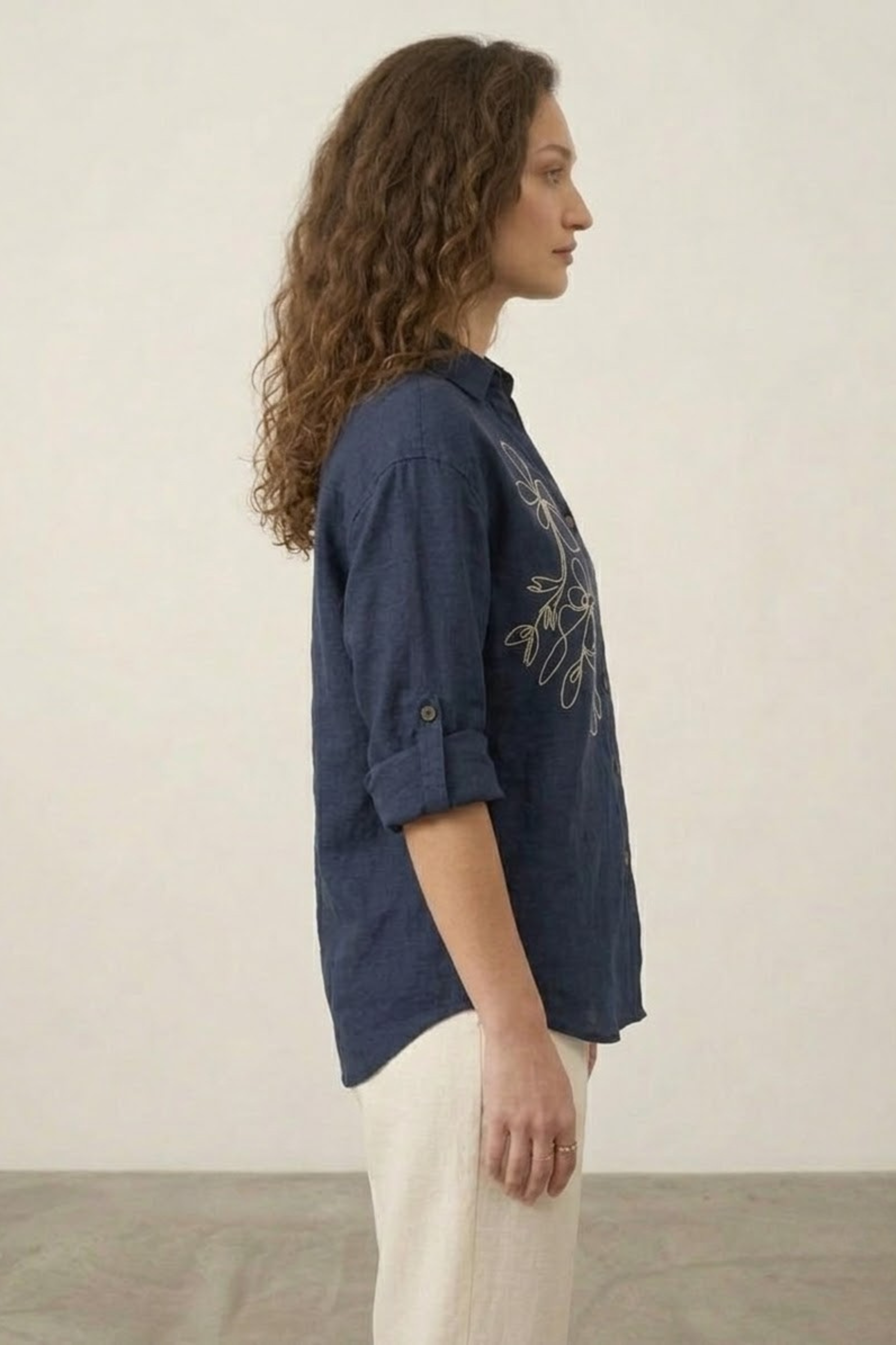 Woman wearing a navy blue shirt with floral embroidery on a plain background