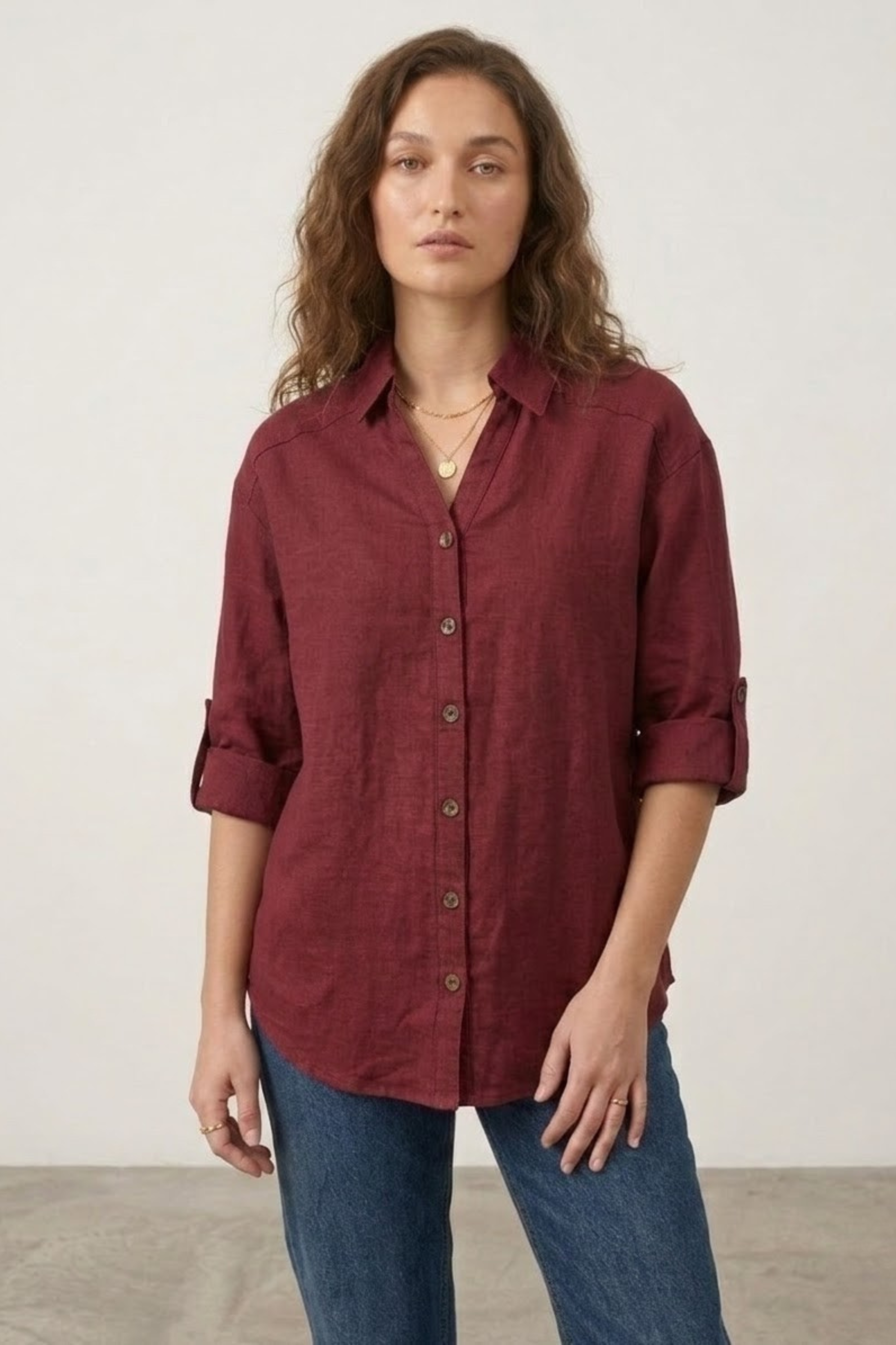 Woman wearing a burgundy shirt and blue jeans against a plain background
