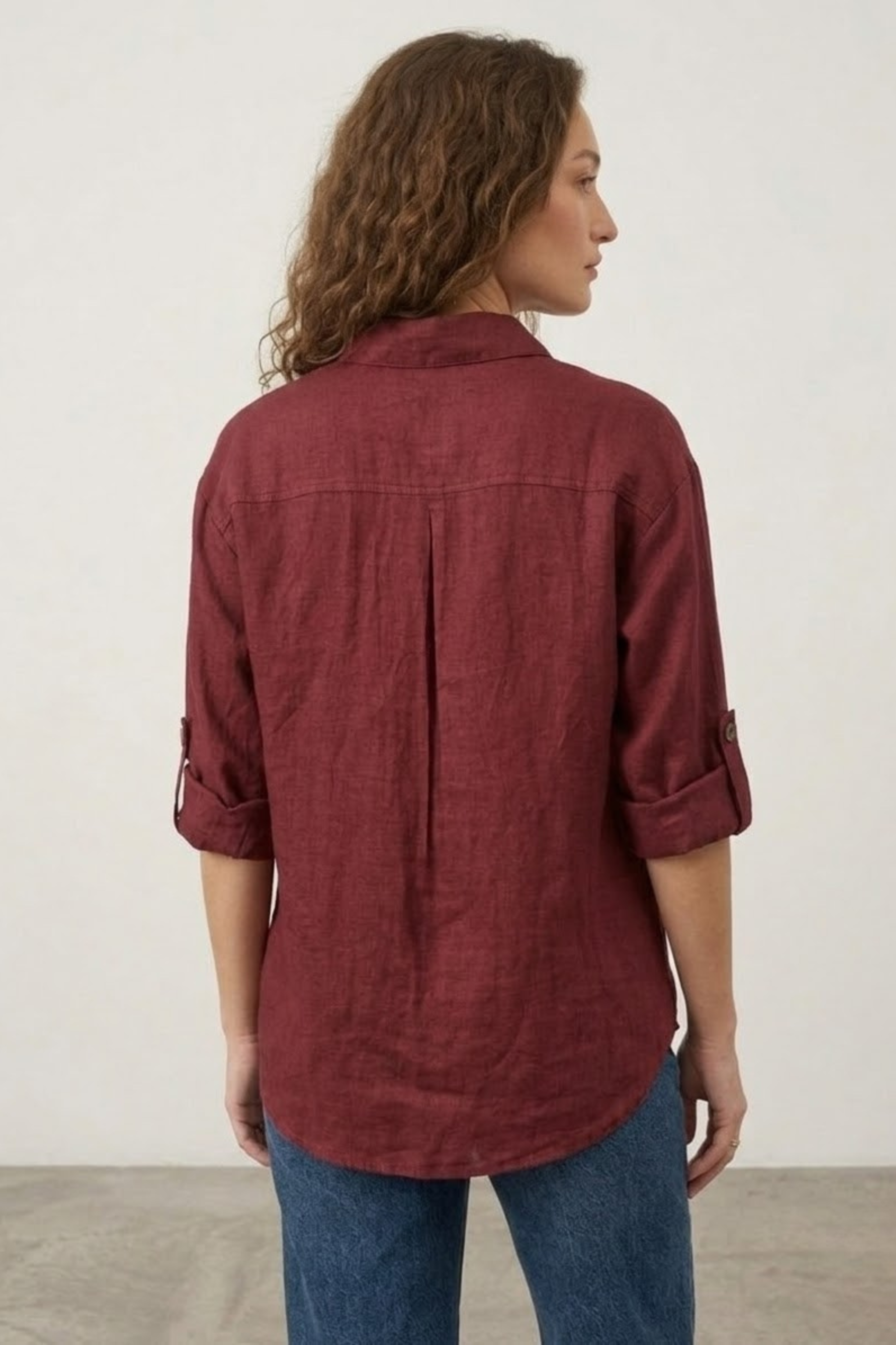 Woman wearing a maroon shirt and blue jeans against a plain background