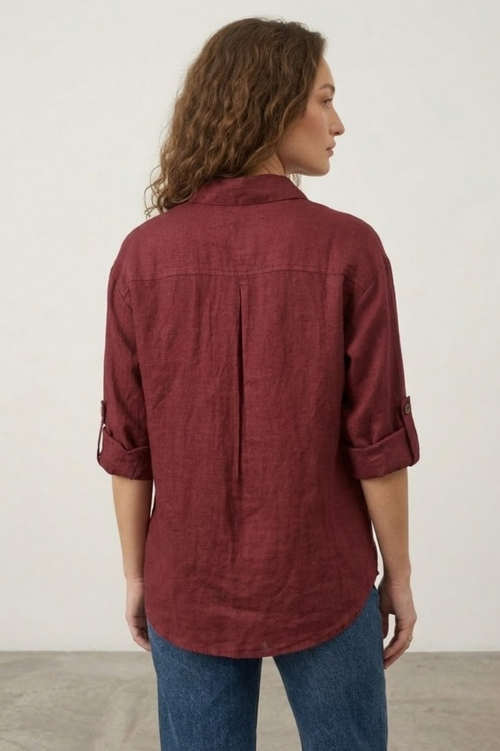 Woman wearing a maroon shirt and blue jeans against a plain background