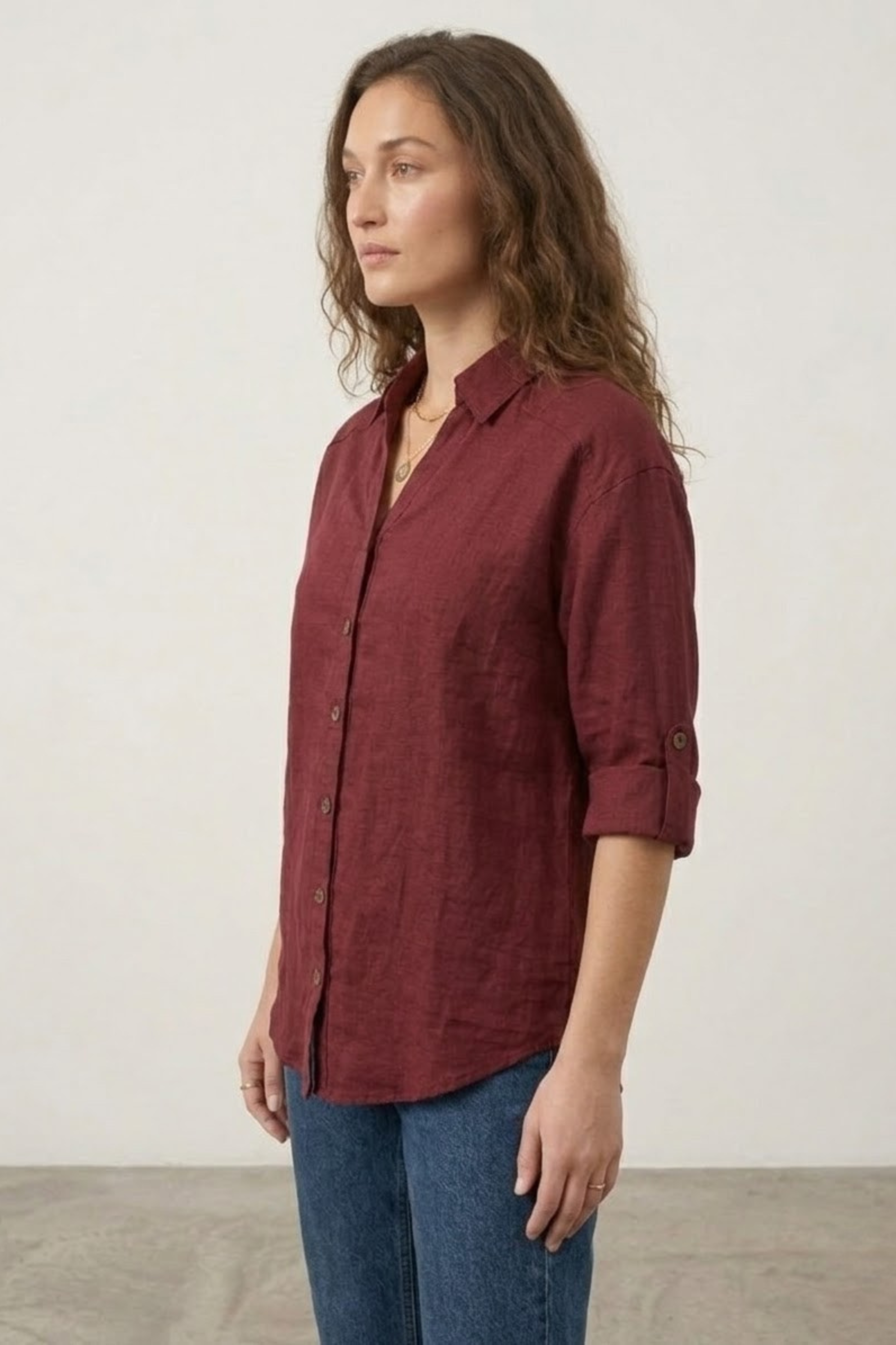 Woman wearing a burgundy shirt and blue jeans against a plain background