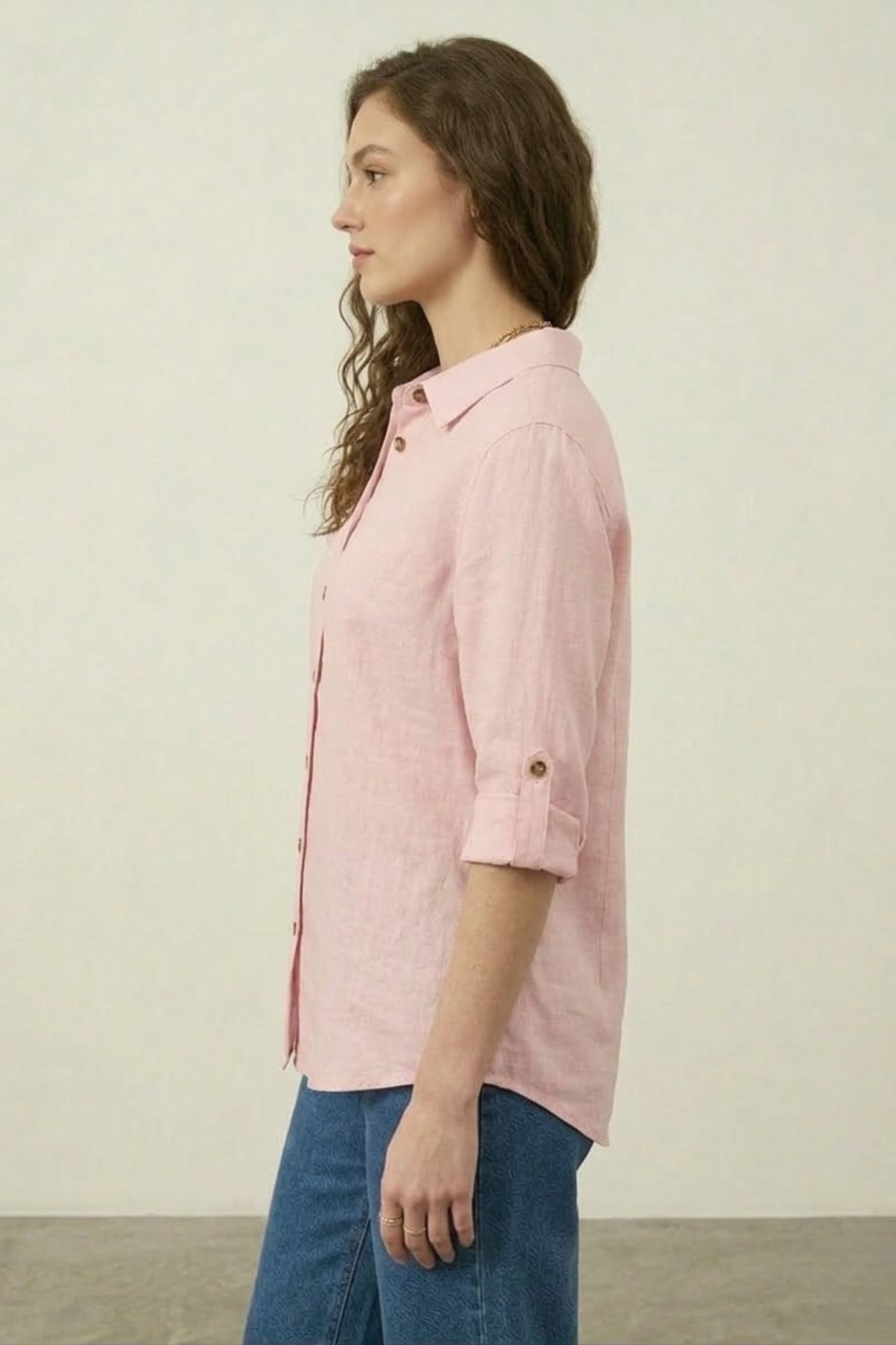 Woman wearing a pink shirt and blue jeans against a plain background