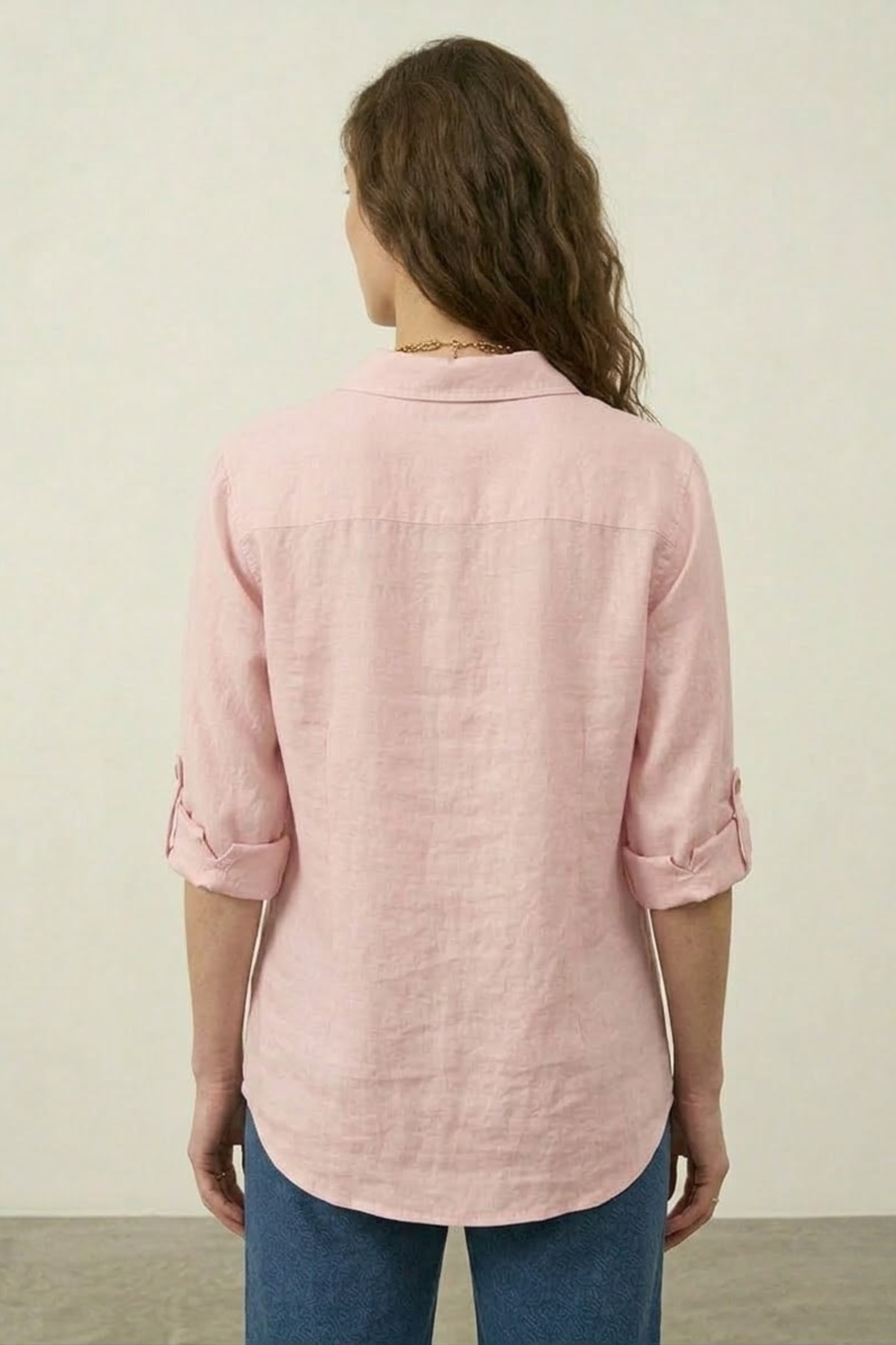 Person wearing a pink shirt with rolled-up sleeves against a plain background