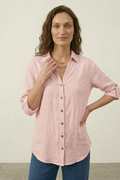 Woman wearing a pink button-up shirt and blue jeans against a plain background