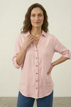 Woman wearing a pink button-up shirt and blue jeans against a plain background