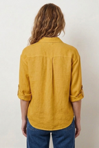 Person wearing a mustard yellow shirt and blue jeans against a white background