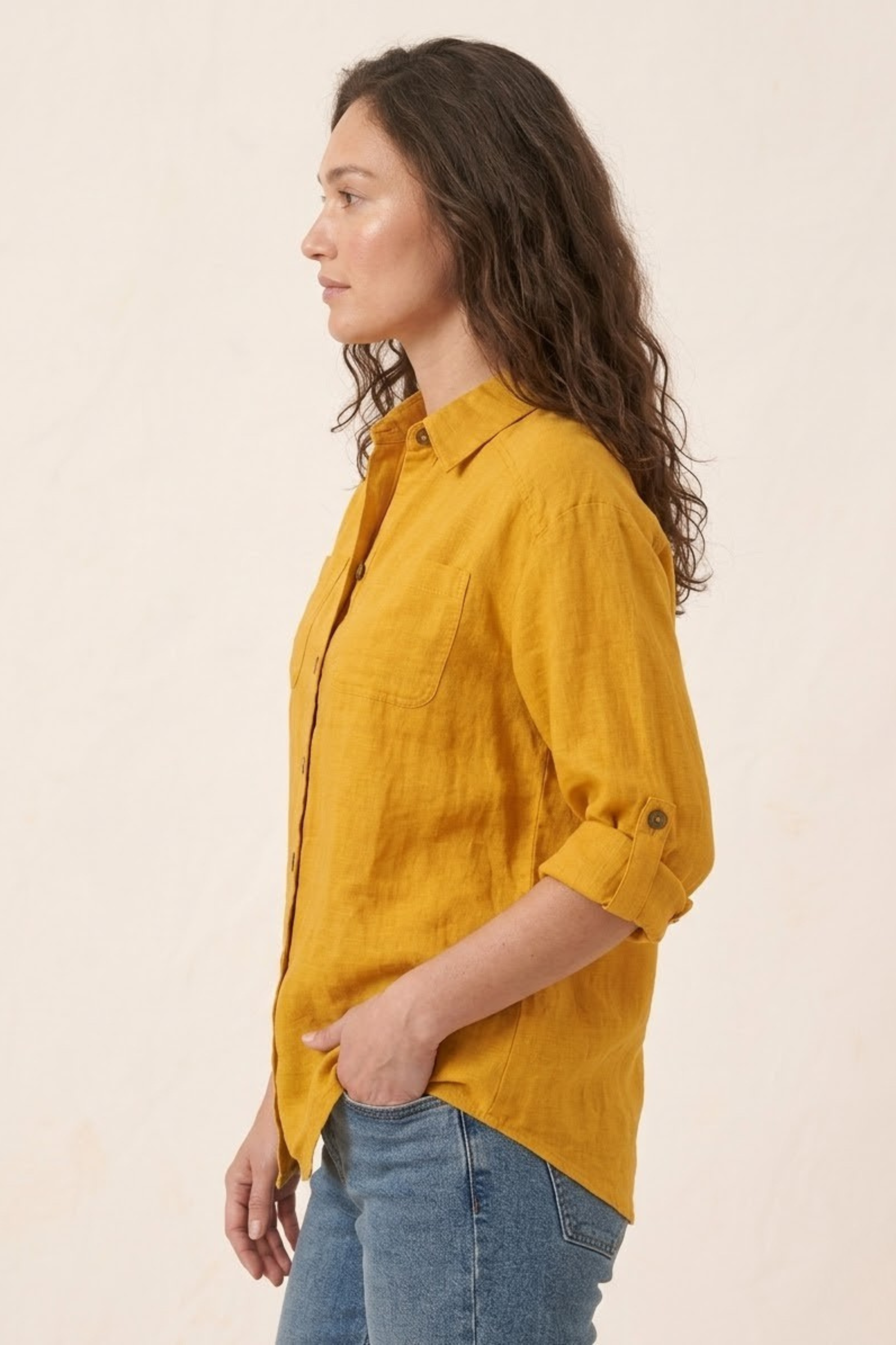 Woman wearing a mustard yellow shirt and blue jeans against a beige background