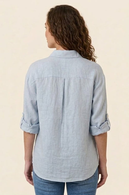 Woman wearing a light blue button-up shirt with rolled-up sleeves on a beige background