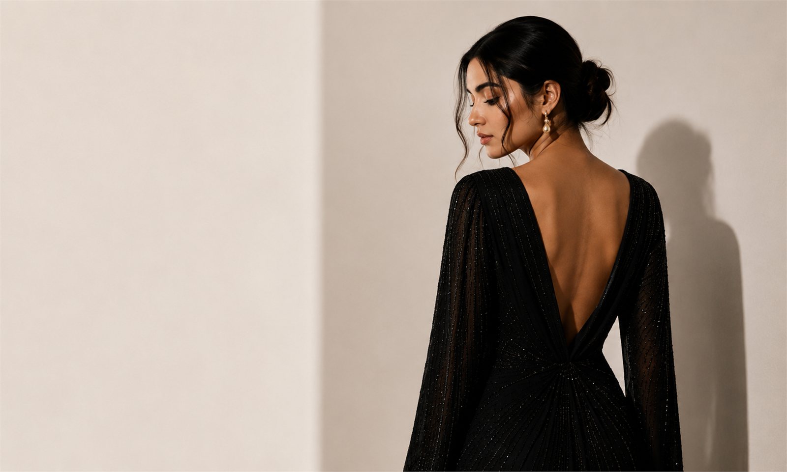 Beaded black gown with an open back, photographed against a plaster wall
